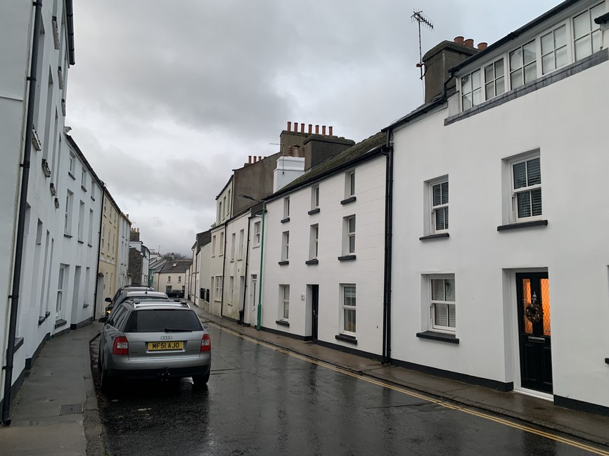 A street view showing a row of white terraced houses on a wet road under an overcast sky with a parked car.
