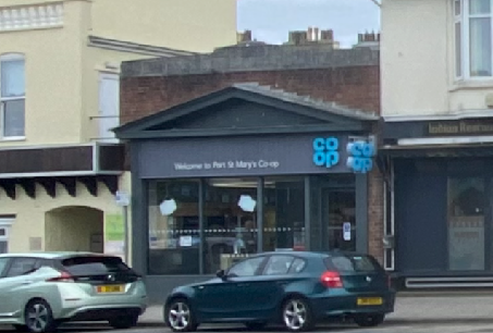 A street-level photograph showing the exterior of a Co-op store with its signage and cars parked in front.