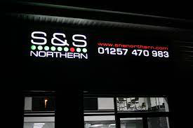 A night-time photograph showing an illuminated sign for 'S & S NORTHERN' with contact details mounted above a building window.