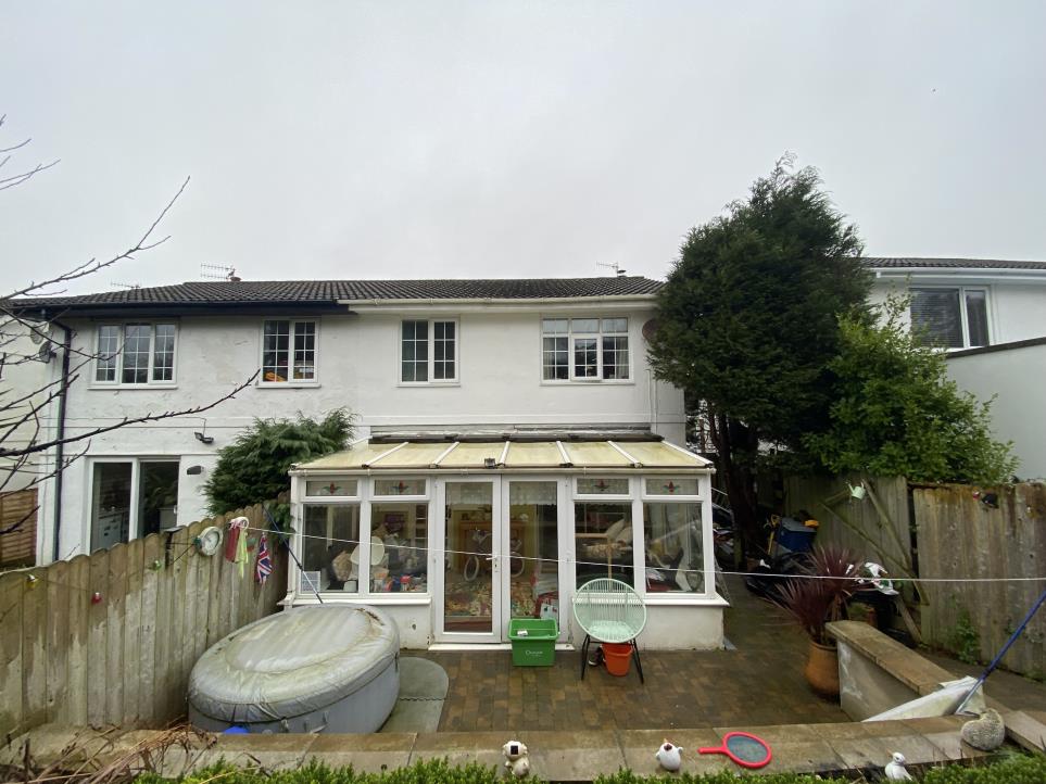 Rear photograph of a white two-story terraced house featuring an existing conservatory and a paved patio area with a hot tub.