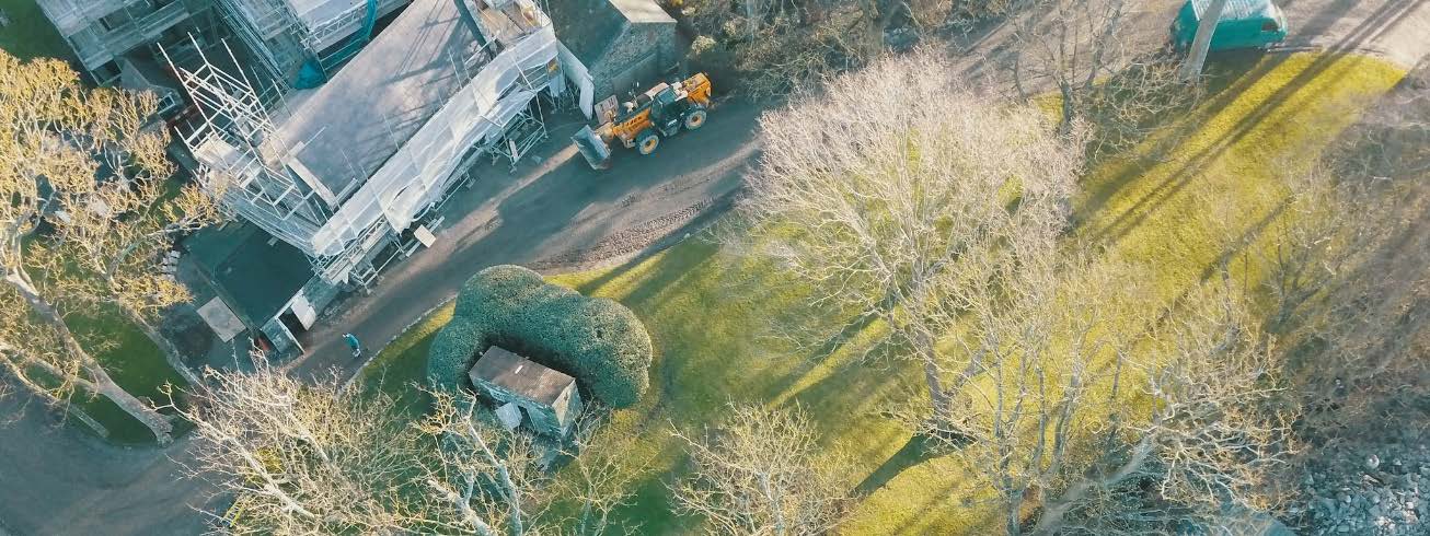 Aerial photograph showing a residential property with a large building covered in scaffolding and a yellow construction vehicle on the driveway.