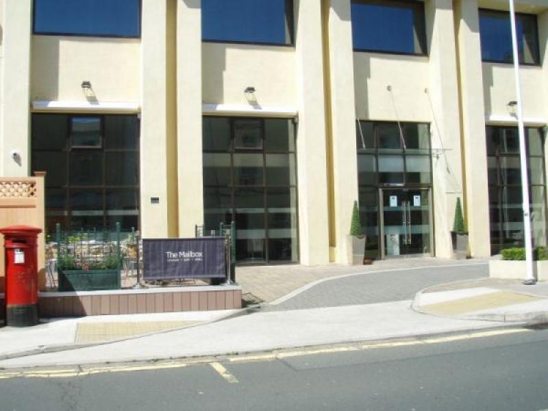 A street-level photograph of a cream-colored commercial building with large ground-floor windows and a sign reading 'The Mailbox'.