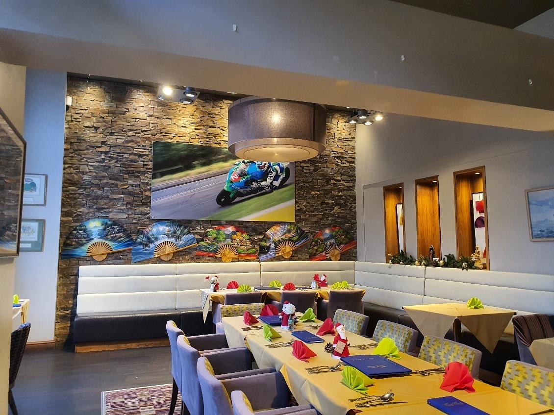 This photograph shows the interior of a restaurant or café with tables set for dining, booth seating, and a stone feature wall displaying motorcycle racing imagery.
