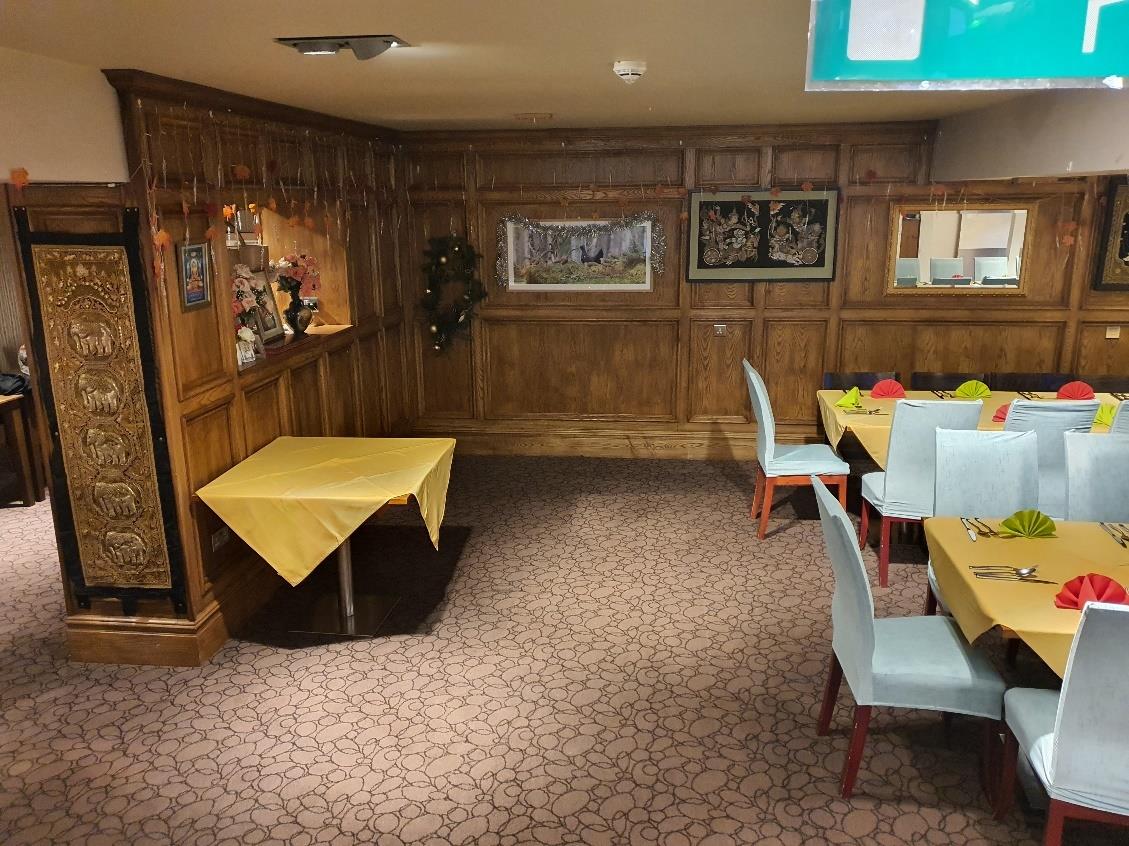 The image displays the interior of a restaurant or dining area featuring extensive wood paneling, patterned carpet, and tables set with yellow tablecloths and light blue chairs.