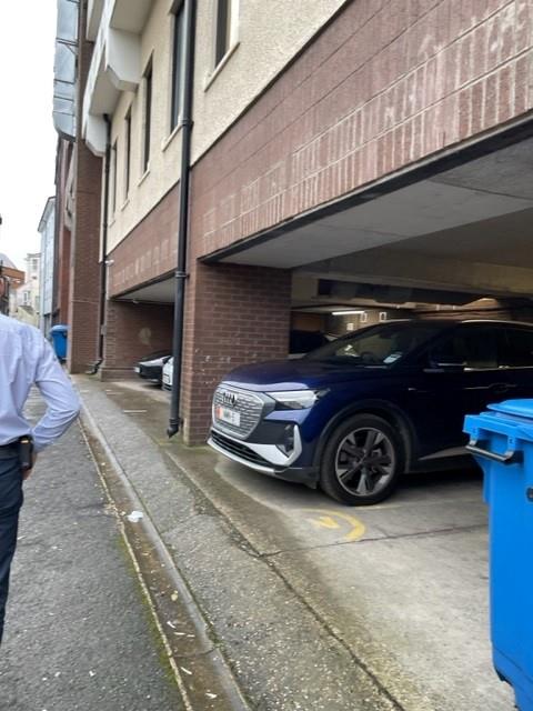 Exterior street-level photograph of a building featuring a covered parking area with a blue car parked underneath.