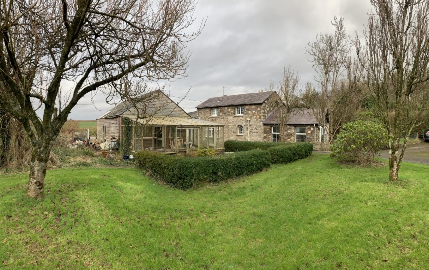 A photograph showing a rural property with a stone house and an adjacent wooden outbuilding structure, likely the existing garage/workshop mentioned in the application.