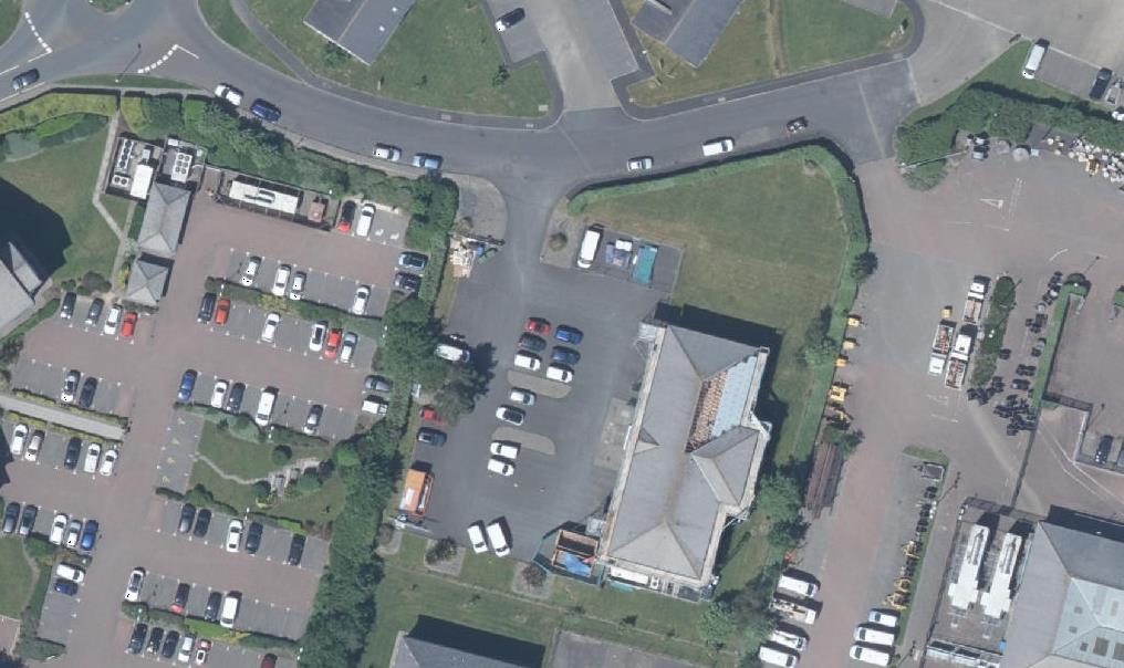 An aerial satellite view showing a large car park, roads, and adjacent commercial buildings.