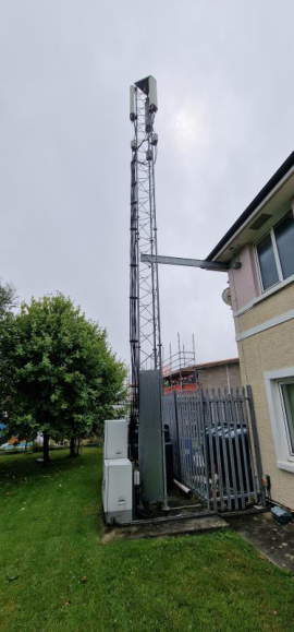 A photograph showing an existing telecommunications lattice tower and ground equipment cabinets situated next to a residential building.