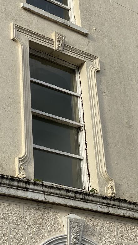 A close-up photograph of an existing building facade, highlighting a tall sash window with decorative molding and rendered walls.