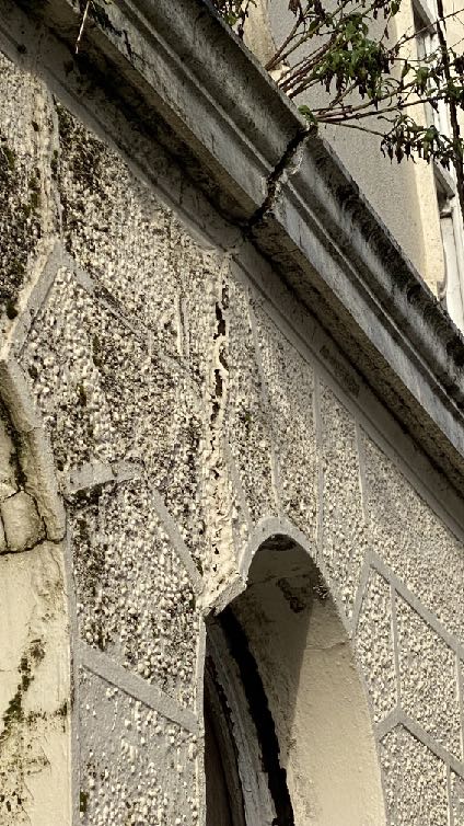 A close-up photograph of a weathered exterior wall featuring pebbledash rendering and stone quoins. An arched opening is visible at the bottom, indicating an older building structure.