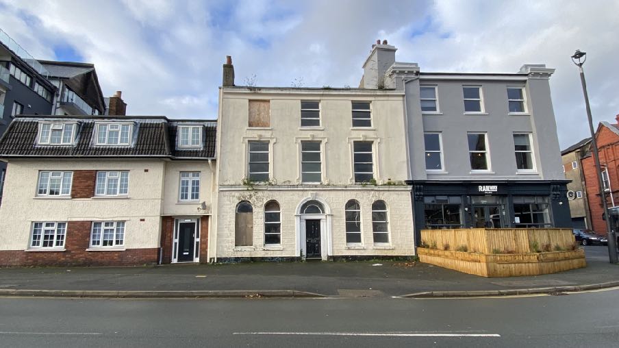 A street-level photograph showing a row of terraced buildings, featuring a central white three-story structure that appears to be the subject of the demolition application.