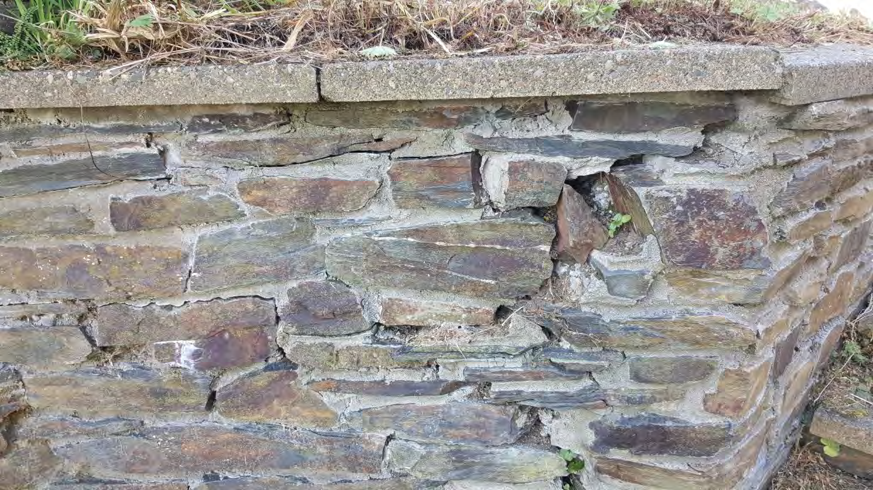 A close-up photograph of a weathered stone retaining wall topped with a concrete coping stone.