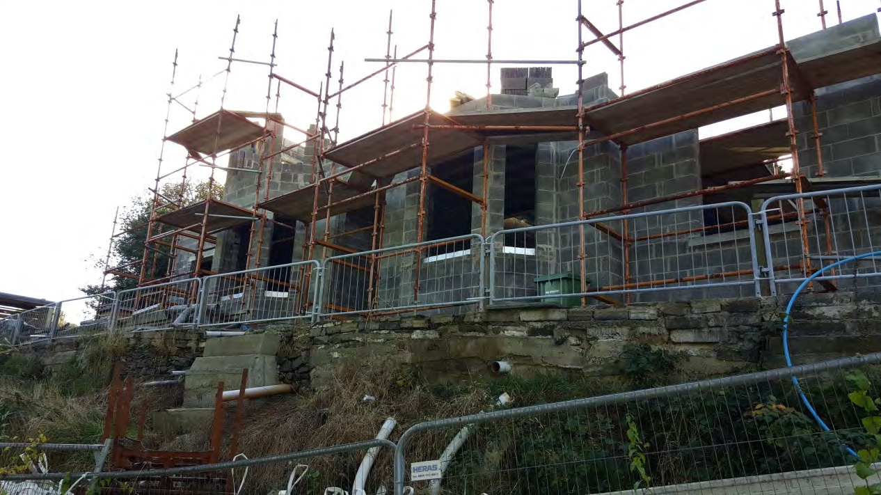 A photograph showing a detached bungalow under construction with grey blockwork walls and extensive scaffolding.