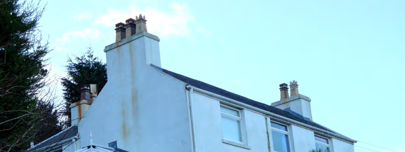 A low-angle photograph showing the upper facade and roofline of a white residential building with a prominent chimney stack and slate roof.