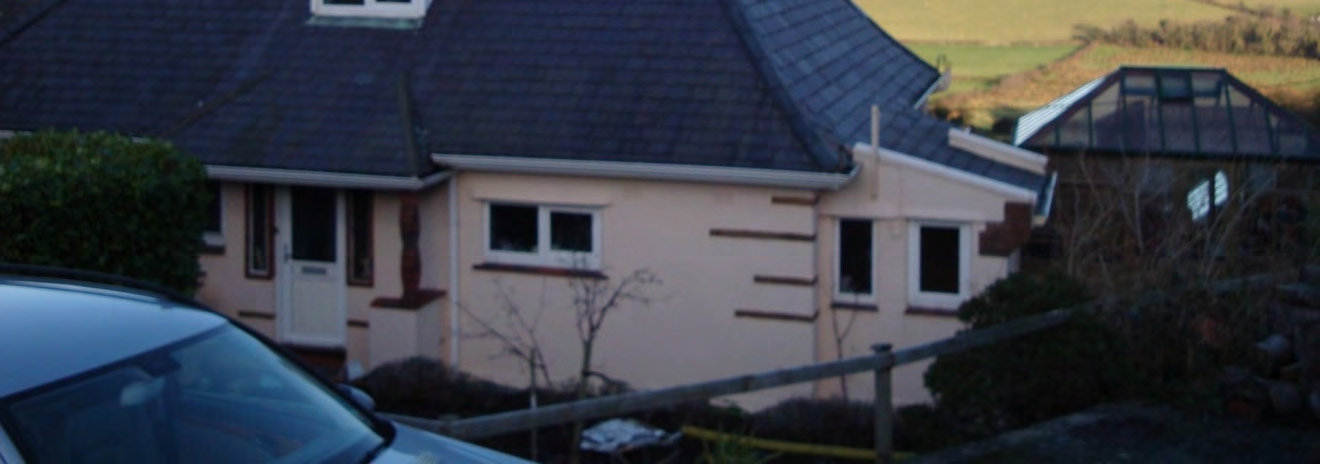 A photograph showing a detached single-storey bungalow with a dark tiled roof and a glass conservatory extension, viewed from a roadside with a car in the foreground.