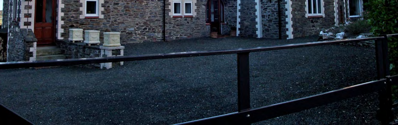 A photograph showing the front elevation of a stone detached house with white quoins and a gravel driveway.