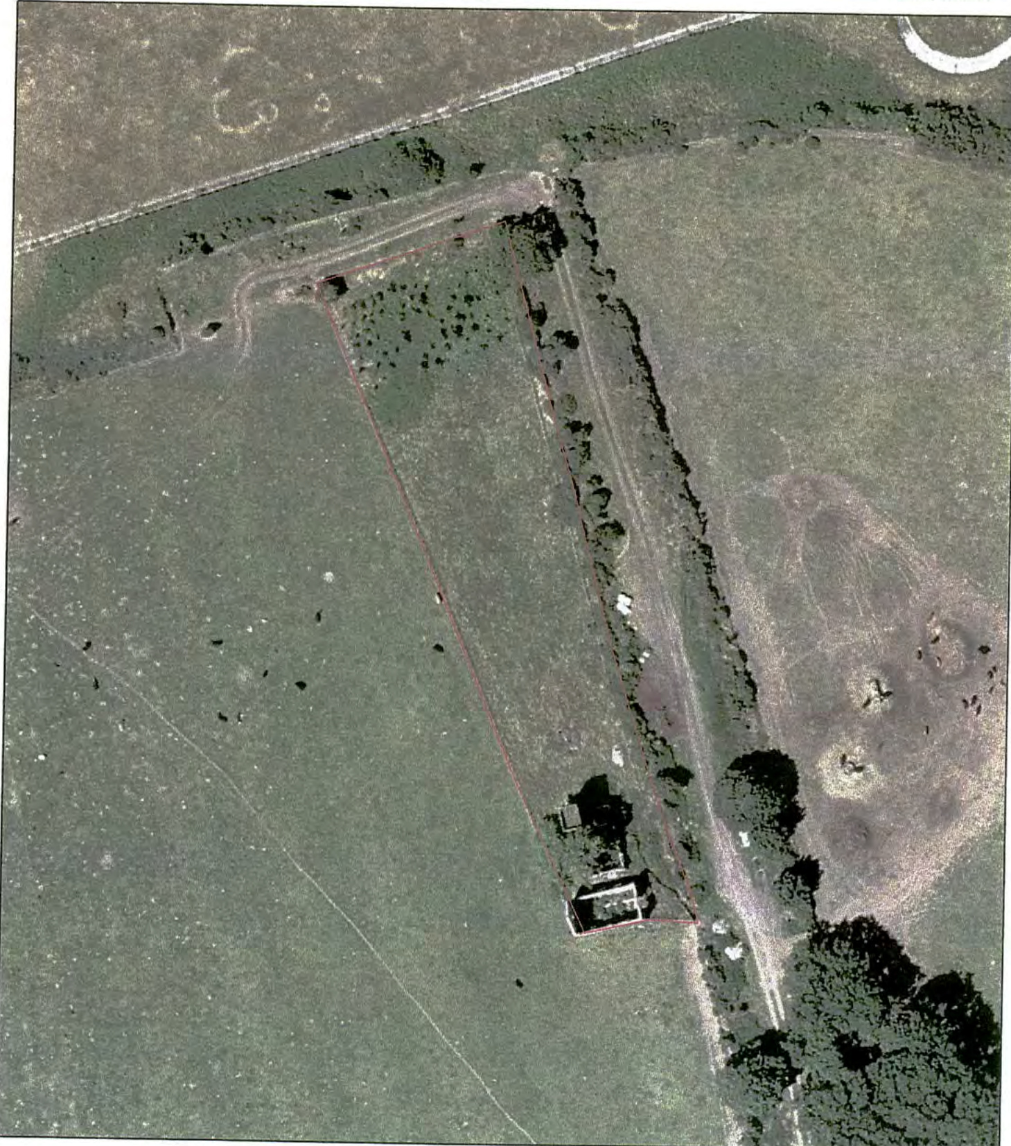 An aerial view of a rural agricultural plot with a red boundary line outlining the site and a small building.