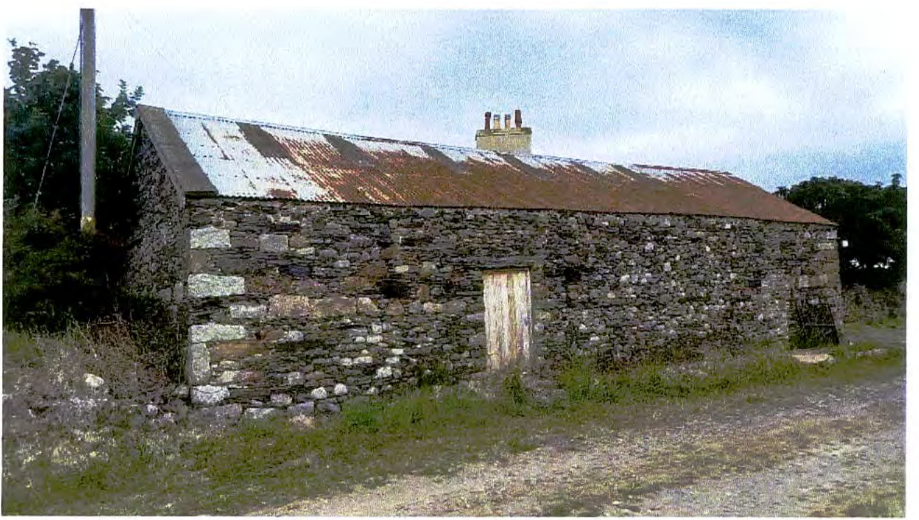 A photograph showing a single-story stone building with a corrugated roof and chimney, situated in a rural setting.
