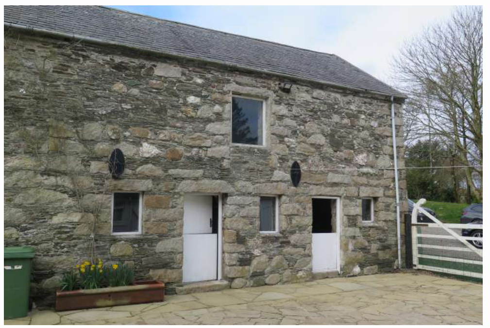 A photograph showing the exterior of a two-story stone barn building with new white windows and doors, set against a rural background.