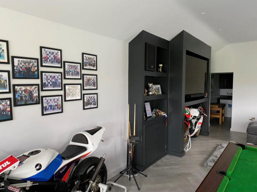 Interior photograph of a converted cow shed showing a leisure room with motorcycles, a pool table, and a large entertainment unit.