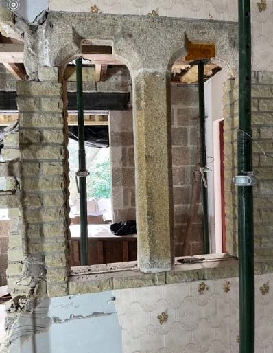 A photograph showing an interior wall with two arched openings under construction, supported by green steel props.