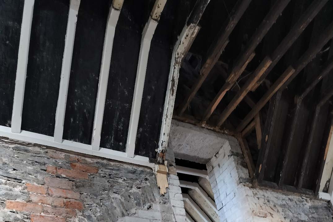 Interior photograph showing exposed wooden roof timbers and stone walls, likely documenting the condition of a historic building prior to renovation.