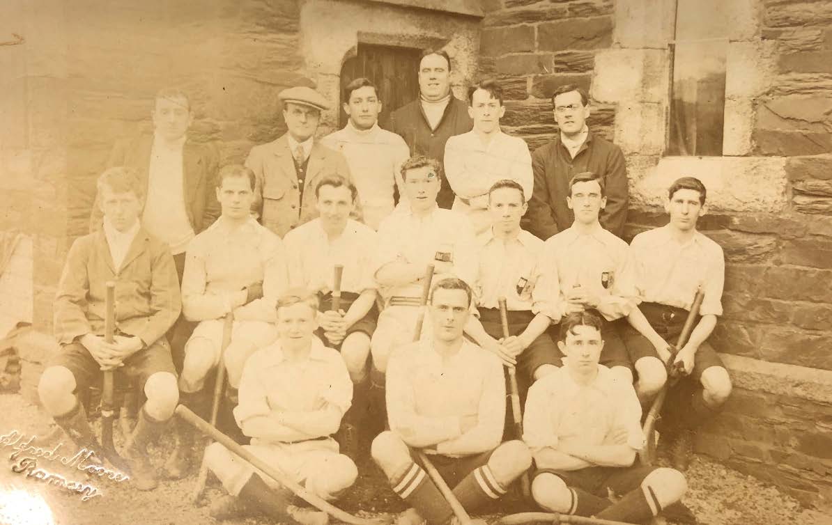 A vintage sepia-toned group photograph of a sports team posing in front of a stone building.