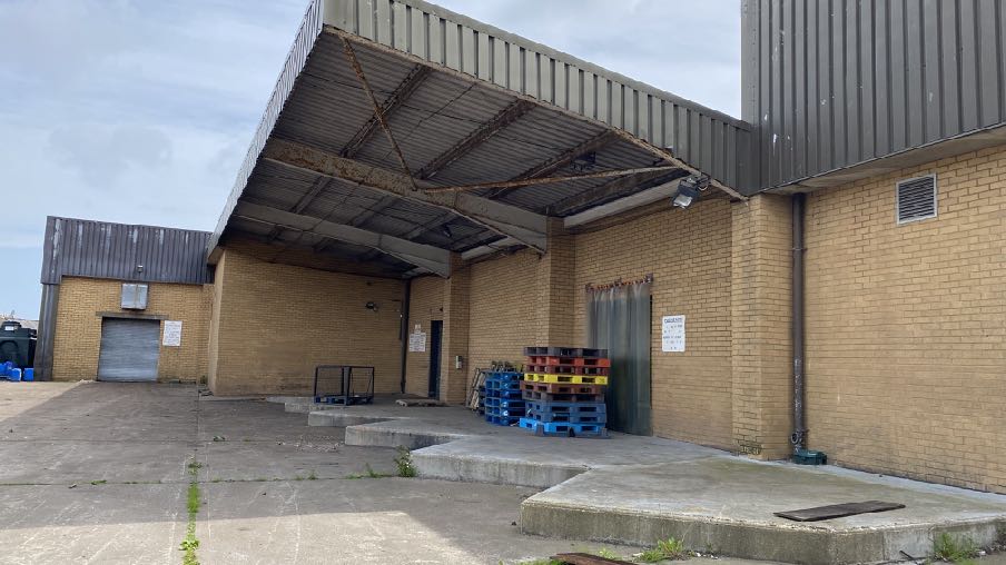 A photograph showing the exterior of a commercial building featuring a large corrugated metal loading bay canopy and concrete apron.