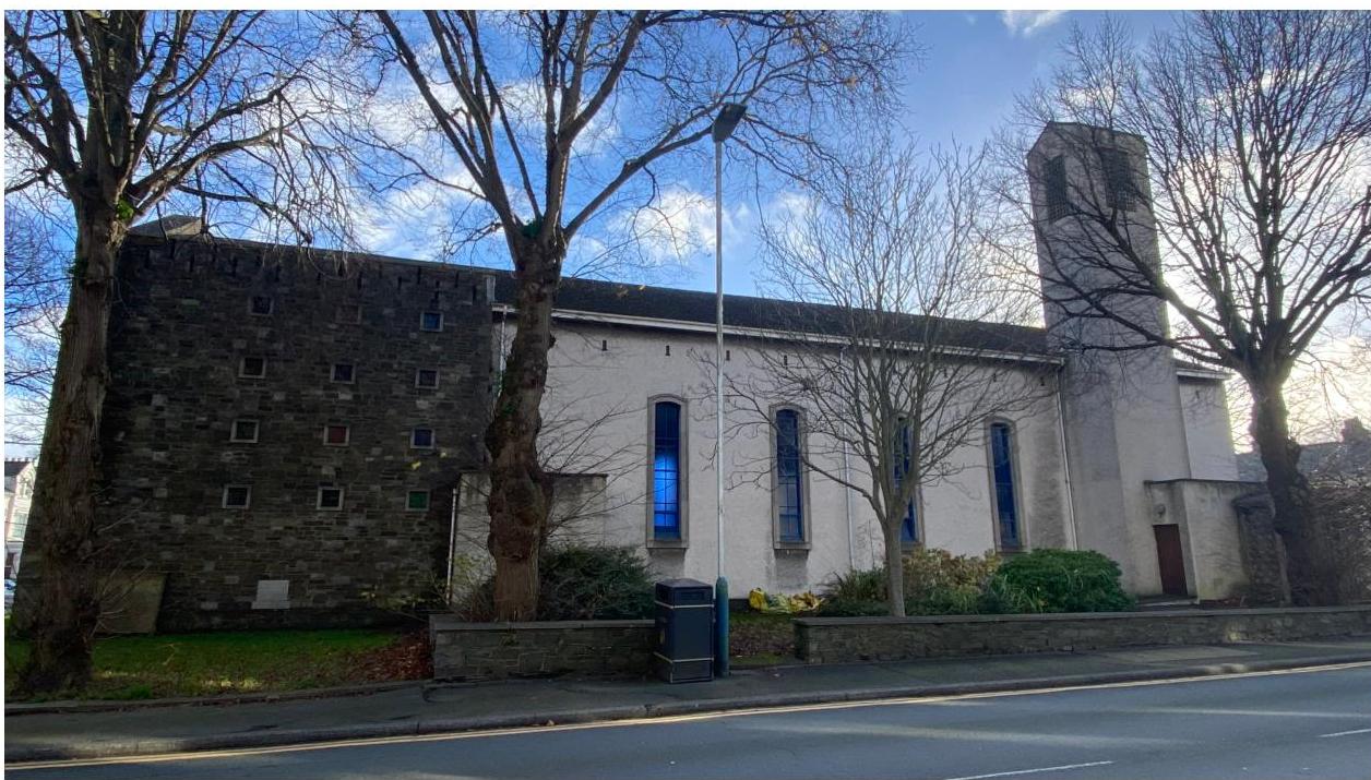 A street-level photograph showing the exterior of a former place of worship with a stone section, white nave, and tower.