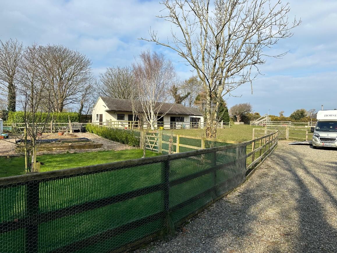 A photograph of a rural property featuring a white single-story building, wooden fencing, and a gravel driveway.