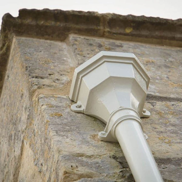 A close-up photograph showing a white drainpipe outlet attached to a rough stone wall with a coping stone at the top.