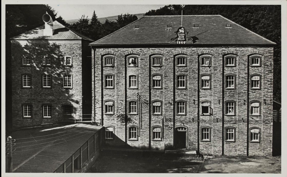 A black and white photograph showing the exterior elevation of a large, multi-story stone mill building with a sign reading 'Laxey Rice Mills 1860'.