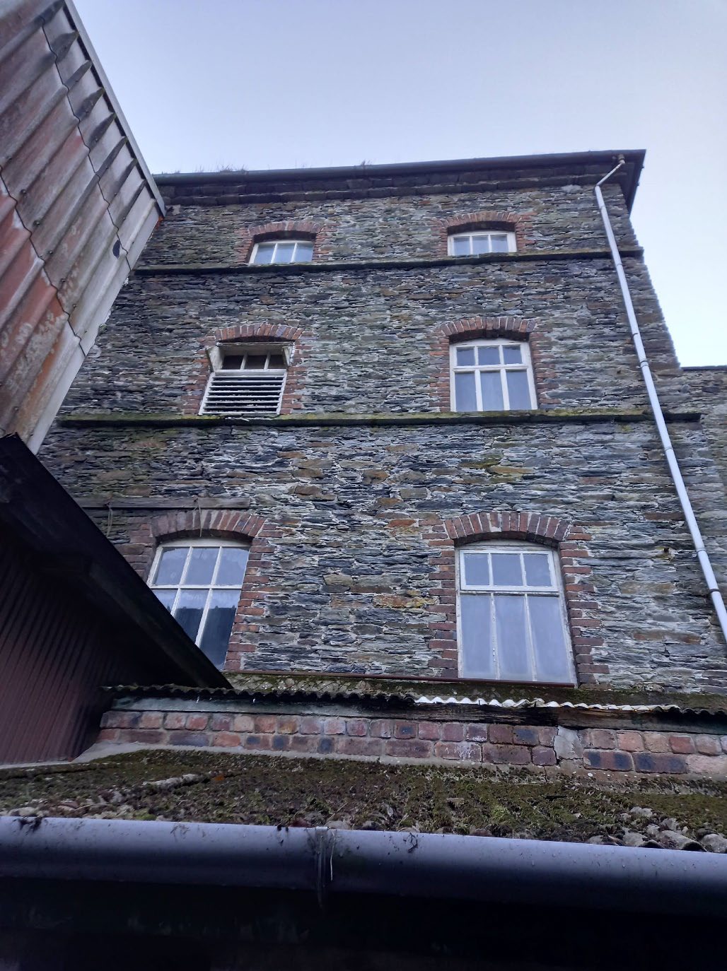 A low-angle photograph showing the stone facade of a multi-story building with brick window arches and white sash windows.