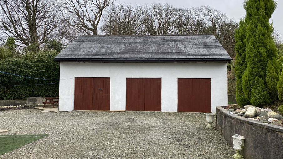 Exterior photograph of a white detached garage with three brown doors and a slate roof.