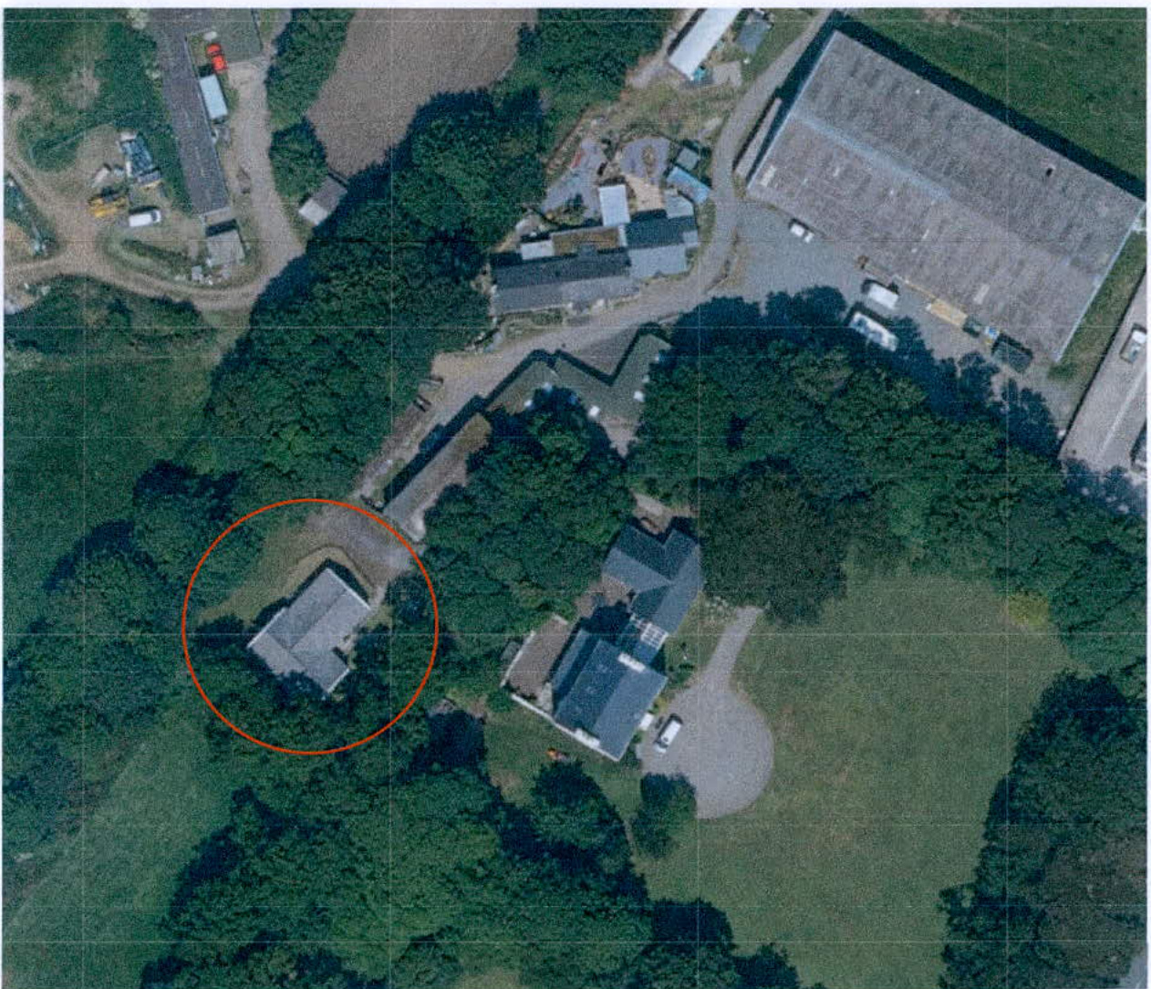 An aerial site location map showing a property highlighted with a red circle, surrounded by trees and adjacent to a larger house and agricultural buildings.