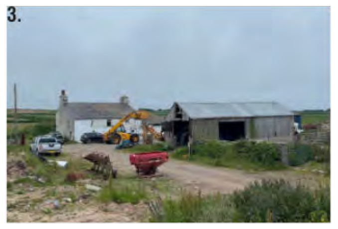 A photograph of a rural farmyard showing an existing white house and a large agricultural barn with machinery and vehicles present.
