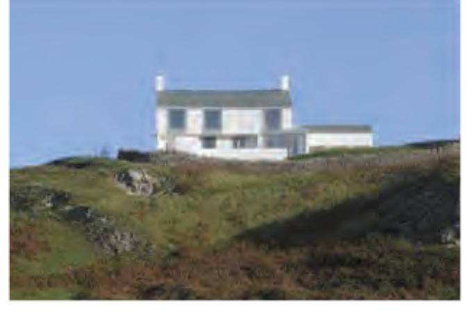 A photograph showing a white two-story building situated on a grassy hillside under a blue sky, likely representing the proposed dwelling.