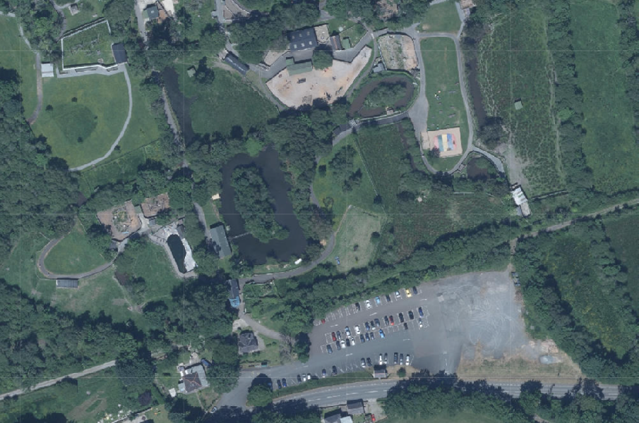 An aerial site plan showing a large paved parking area surrounded by green fields and trees.