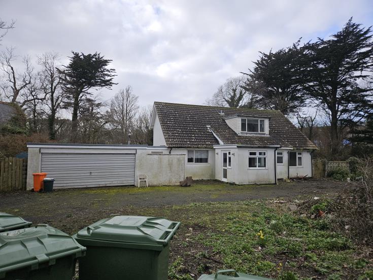 A photograph of the existing property showing a white detached bungalow with an attached garage and surrounding garden area.