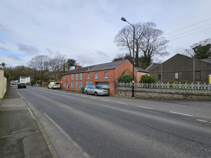 A street-level photograph showing the existing long, orange-painted building on Mill Road, which is the subject of the proposed demolition and replacement application.
