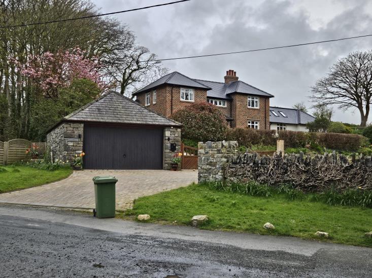 A street-level photograph showing a large two-story brick detached house with a slate roof and a stone garage with a paved driveway.