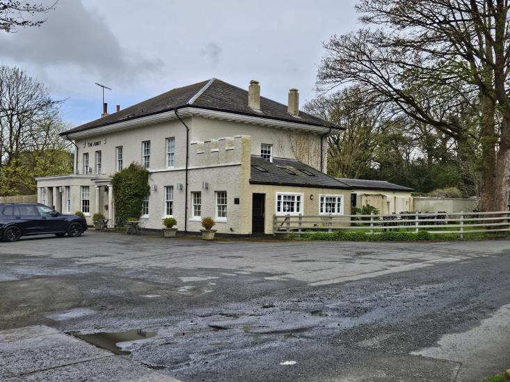 A photograph of a large white detached house with a slate roof, situated on a rural site with a paved driveway and parked car.