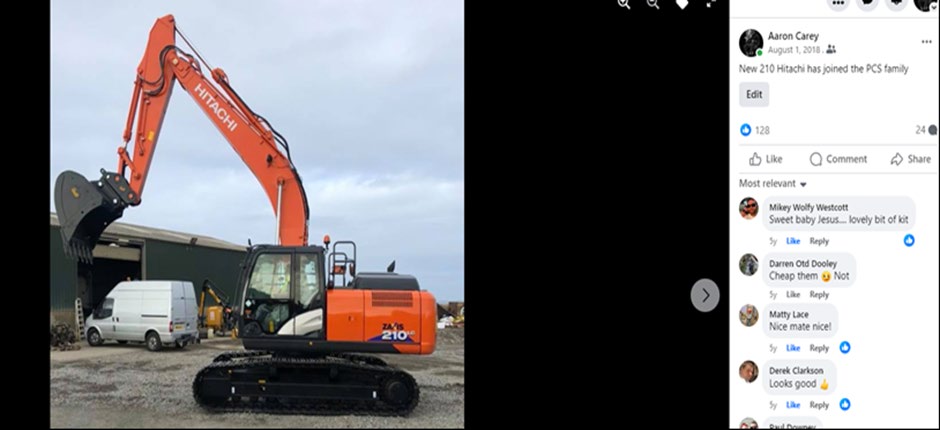 A photograph showing a large orange Hitachi excavator parked on a gravel yard outside a green industrial workshop building with a white van nearby.