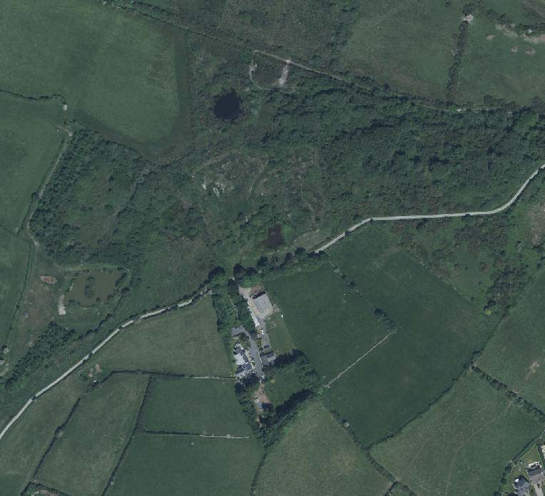 Aerial view of a rural property surrounded by green fields and hedgerows, showing the site location relative to the road.