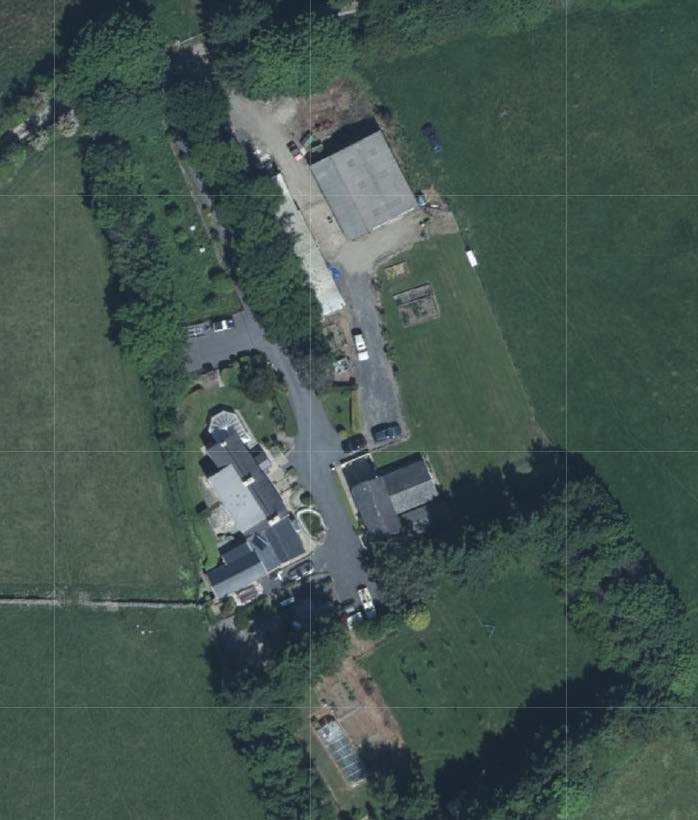 An aerial site plan showing a rural property with a main dwelling, a large barn-like outbuilding, and surrounding green fields.