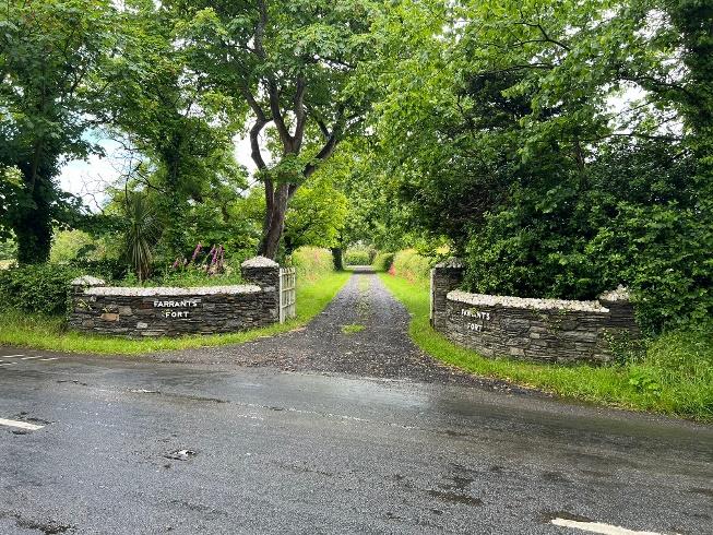 A photograph showing a rural property entrance with stone gate piers and a gravel driveway leading into a wooded area.