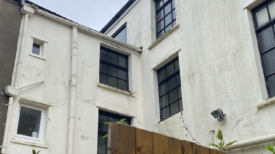 Exterior photograph of a white-washed building featuring large multi-paned windows, likely a converted barn or industrial structure.