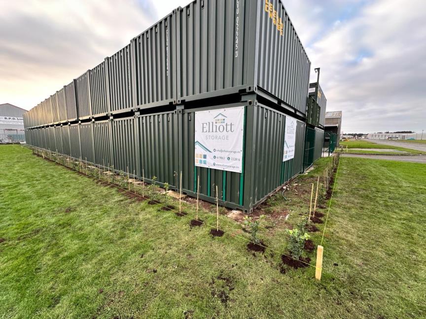 A photograph showing the exterior of a self-storage facility constructed from stacked shipping containers with landscaping in the foreground.