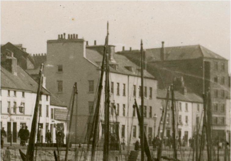 A vintage black and white photograph showing a street scene with multi-story buildings and boat masts in the foreground.