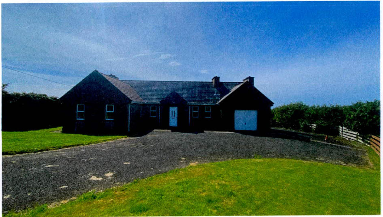 A photograph of a single-story detached bungalow with an attached garage, situated in a rural setting with a gravel driveway.